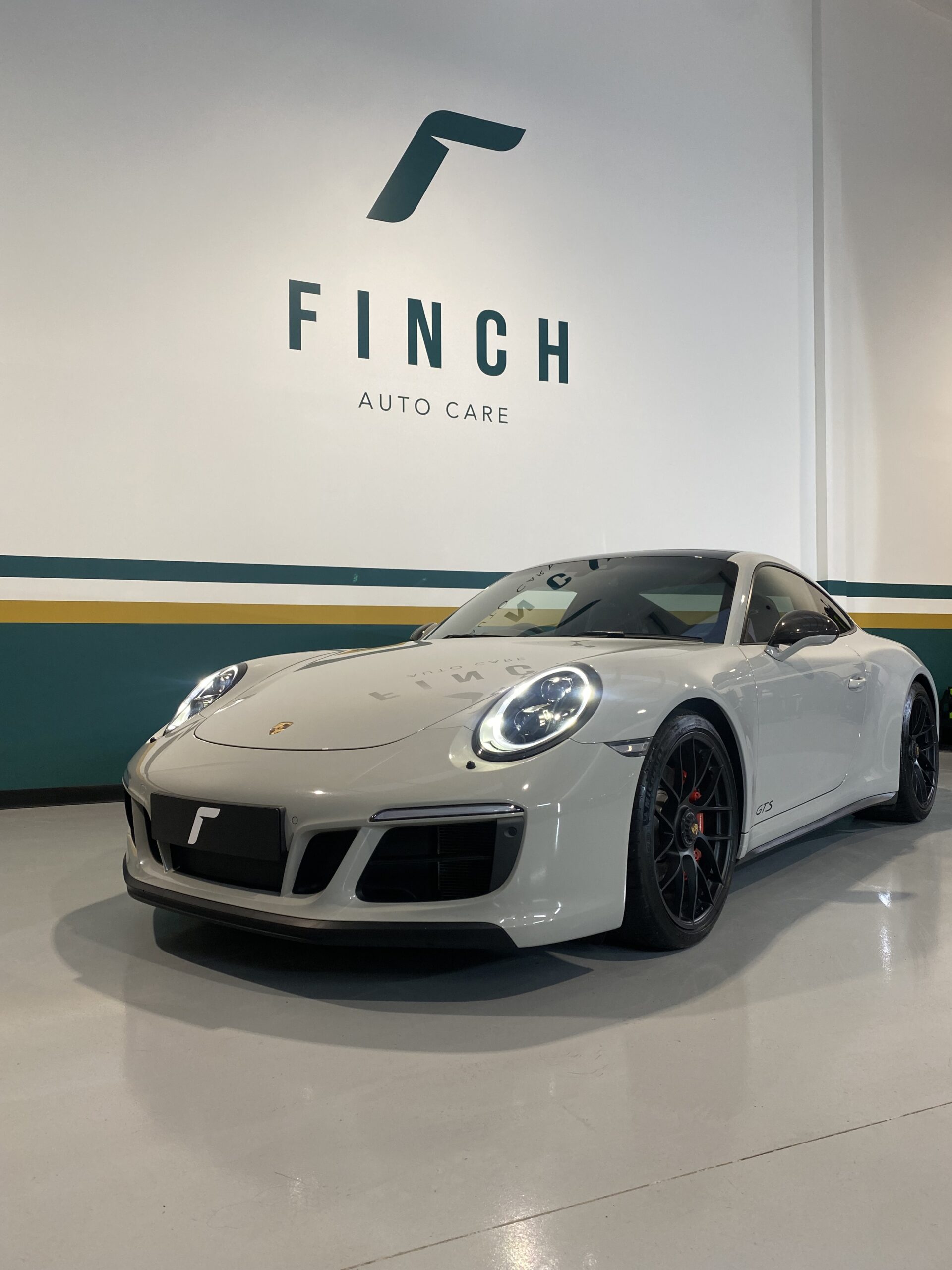 A white porsche parked inside a facility with "finch auto care" written on the wall.