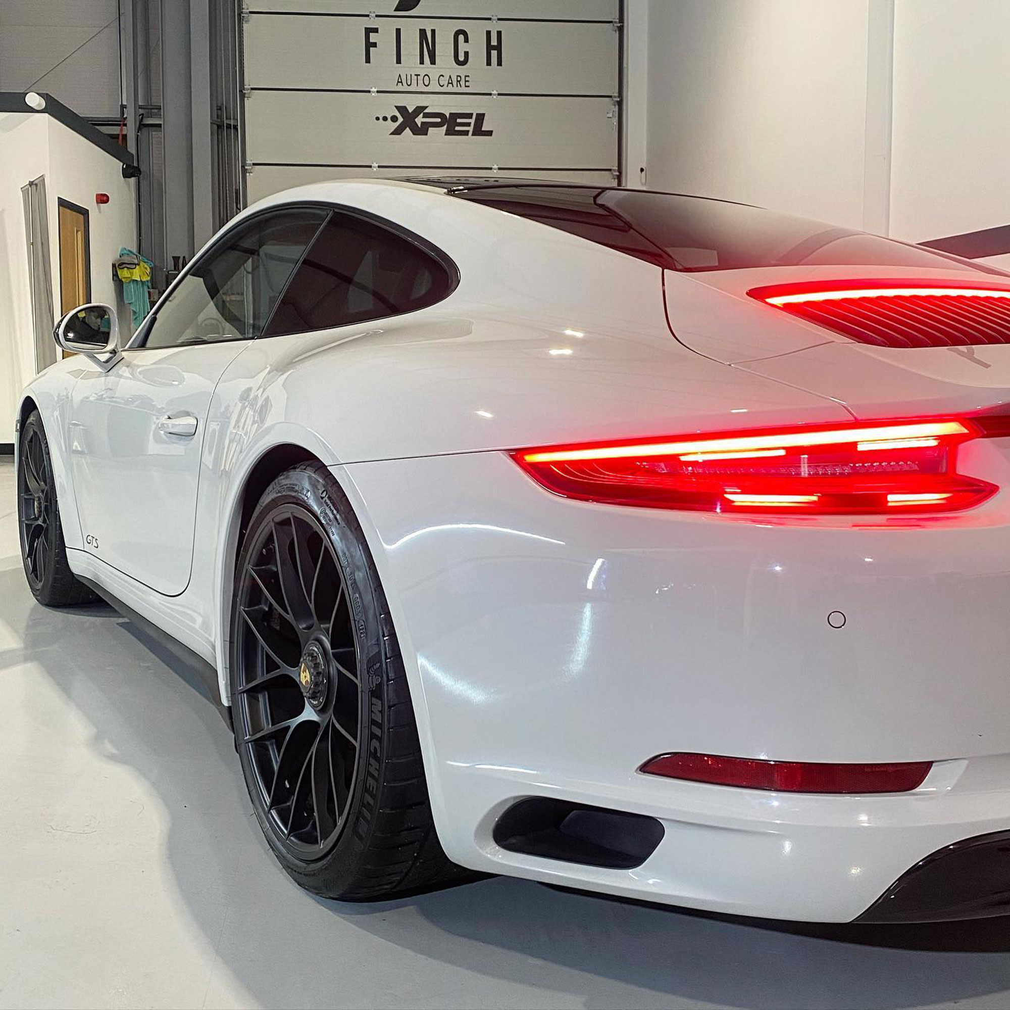 White porsche 911 with distinctive tail lights parked in an auto care workshop.