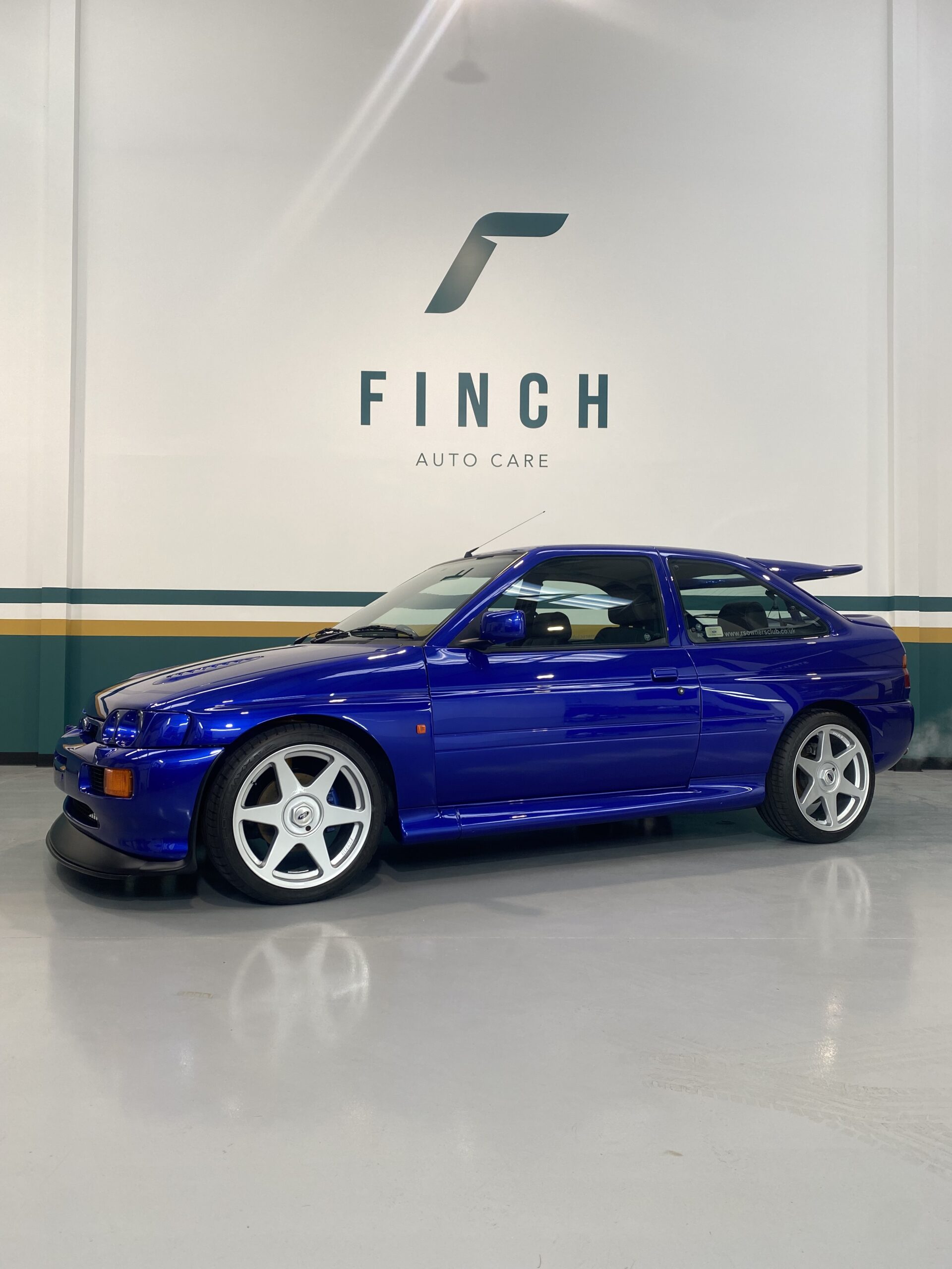 A blue sports car parked inside a detailing shop with the logo "finch auto care" on the wall behind it.