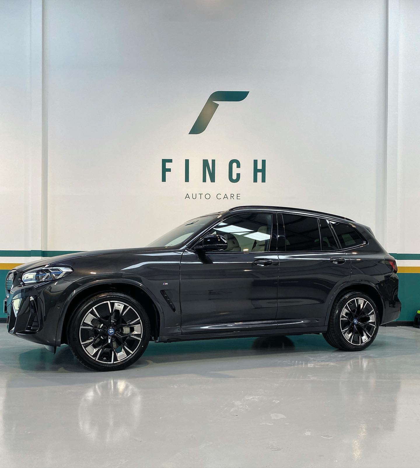 A black luxury suv parked inside a clean and modern vehicle service center with the signage "finch auto care" on the wall behind it.