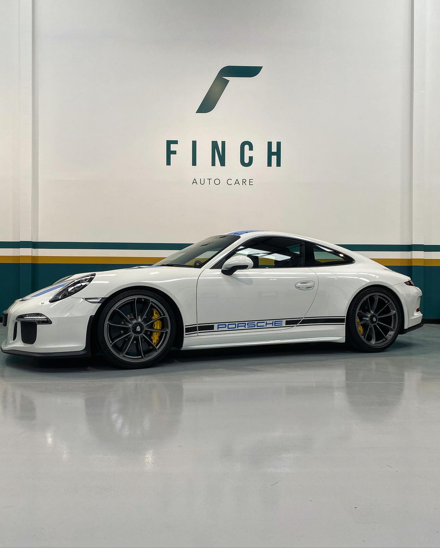 A white porsche 911 parked inside an auto care facility with the logo "finch" on the wall in the background.