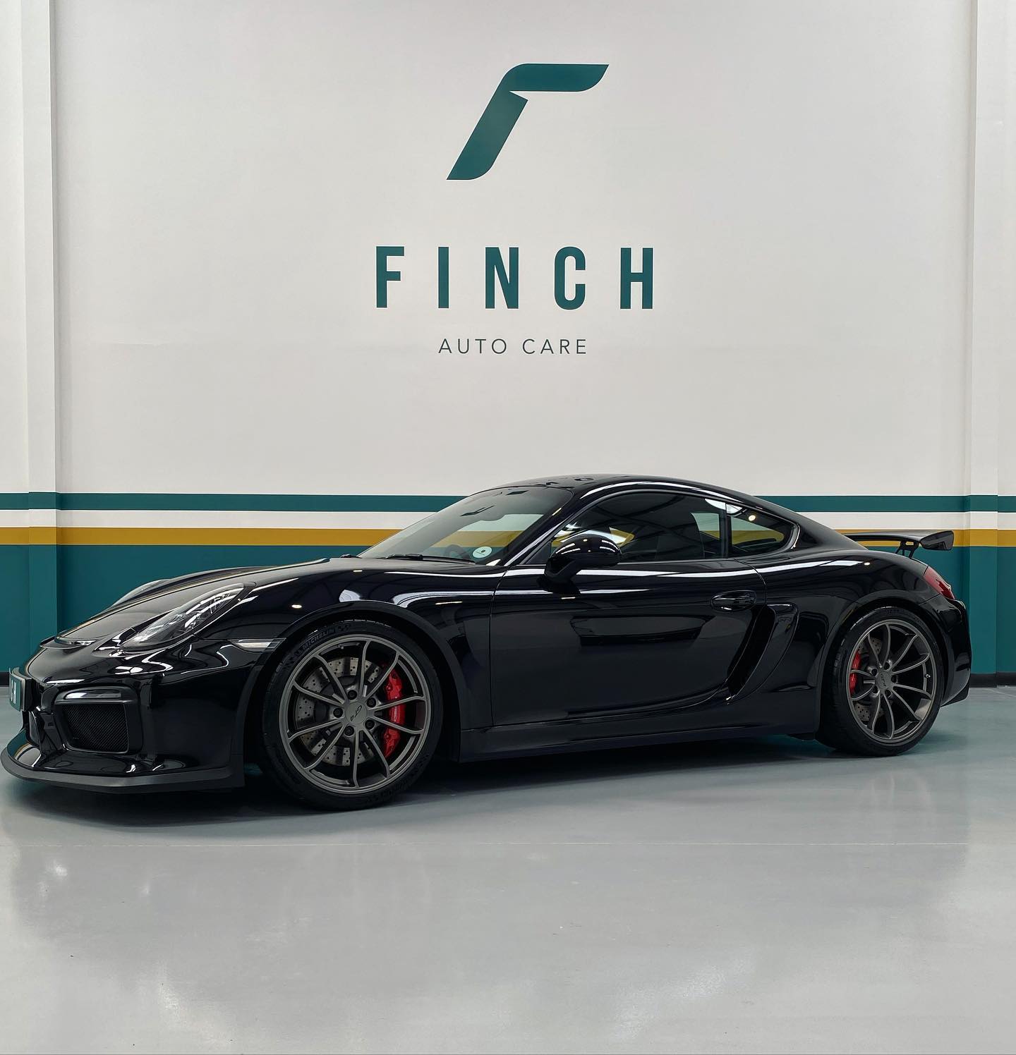 A black sports car parked inside a facility with "finch auto care" sign on the wall.