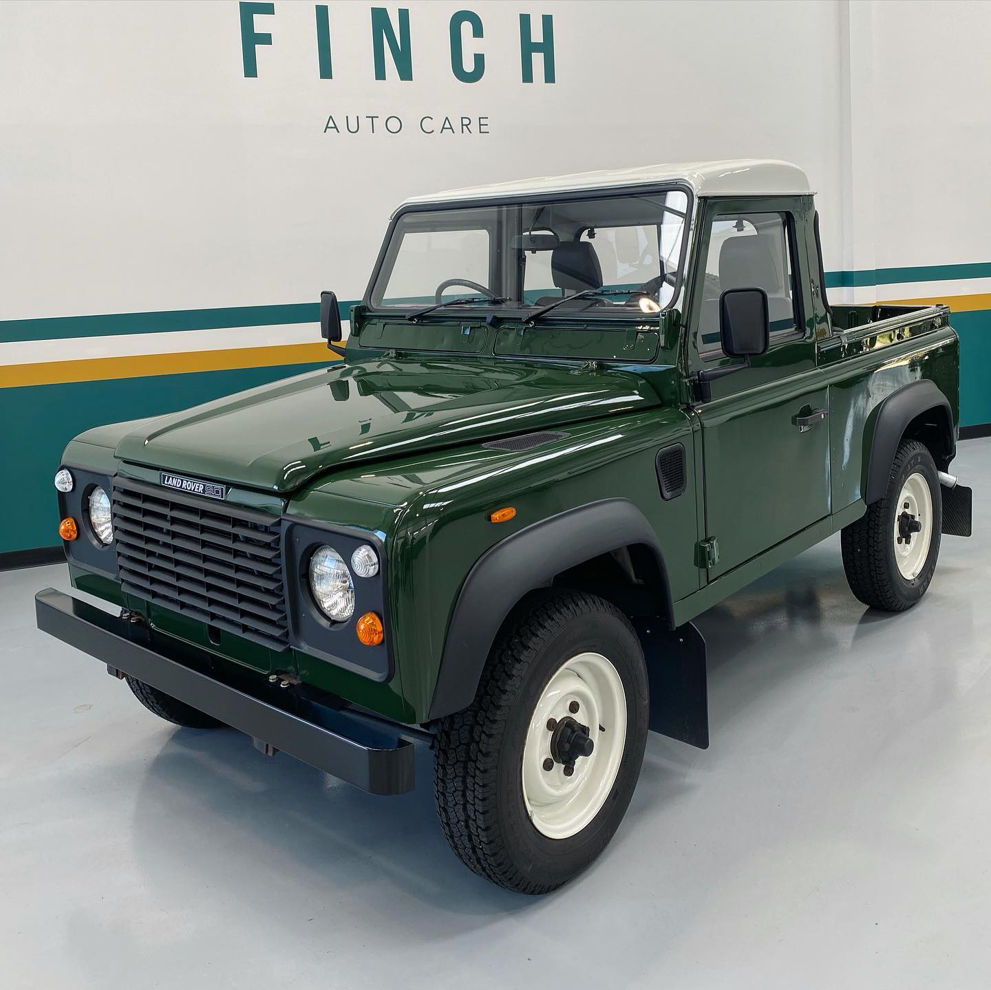 Green land rover defender pickup in a showroom setting.
