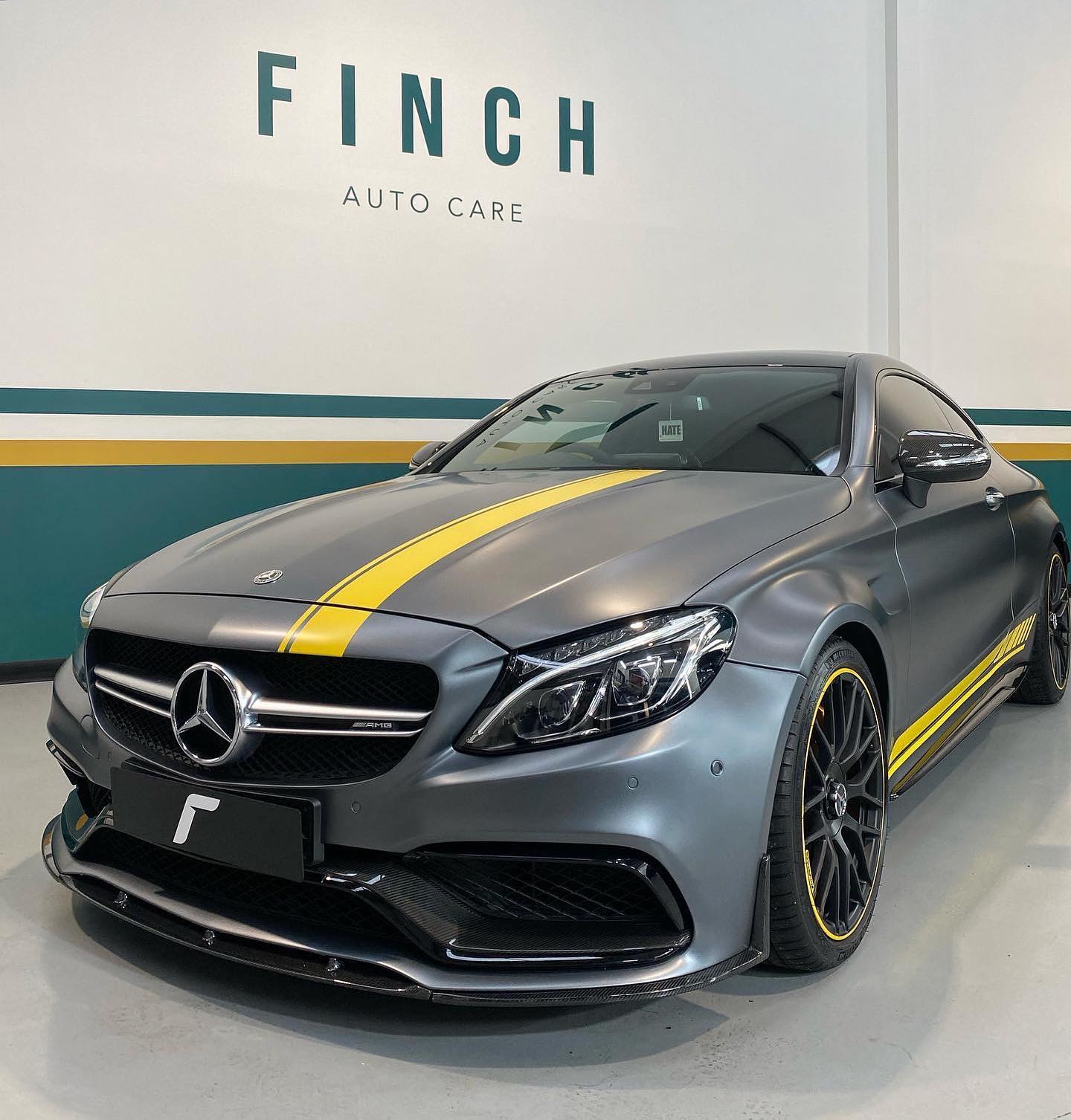 A mercedes-benz coupe with custom yellow accents parked in front of the finch auto care sign.