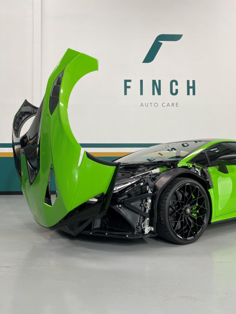 Green sports car with door open in auto care facility.