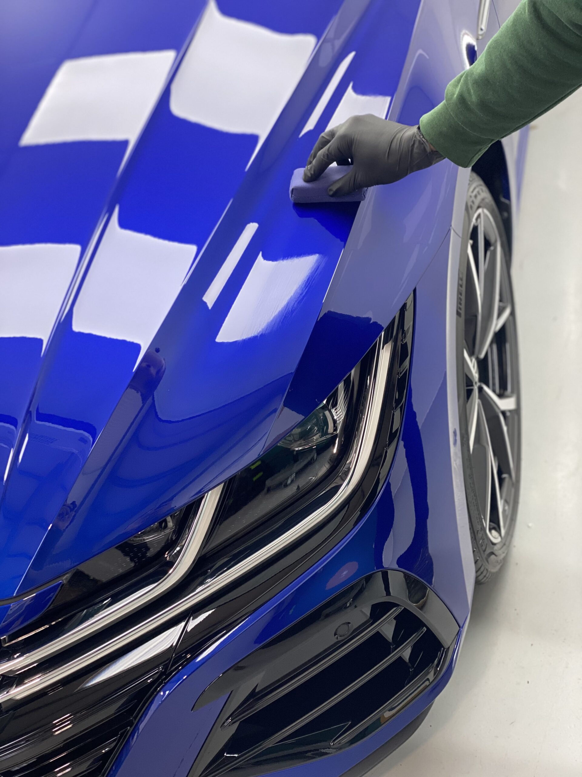 Person in a glove touching the hood of a shiny blue car.