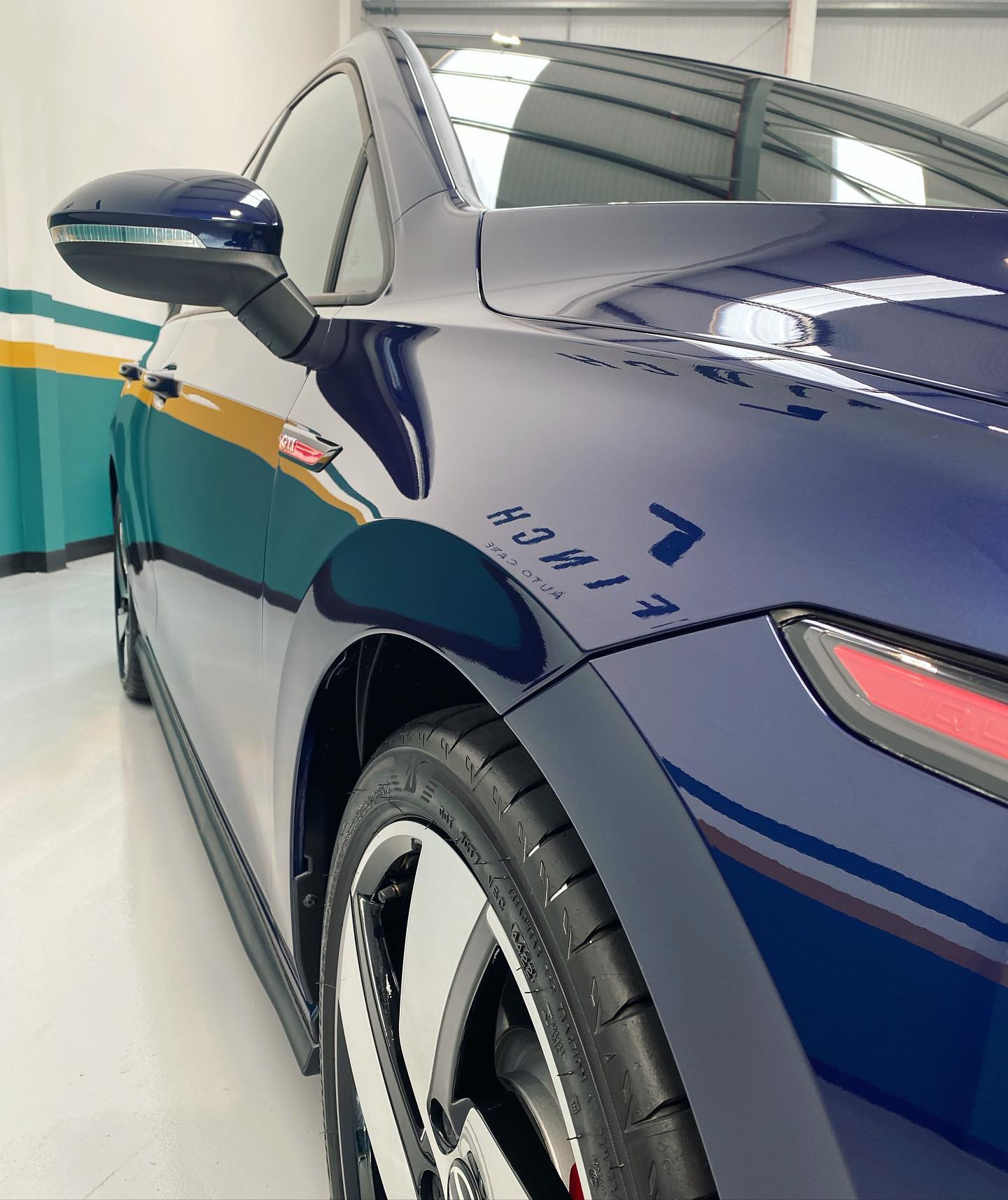Side view of a blue electric car with aerodynamic design, highlighting the rear mirror and wheel.