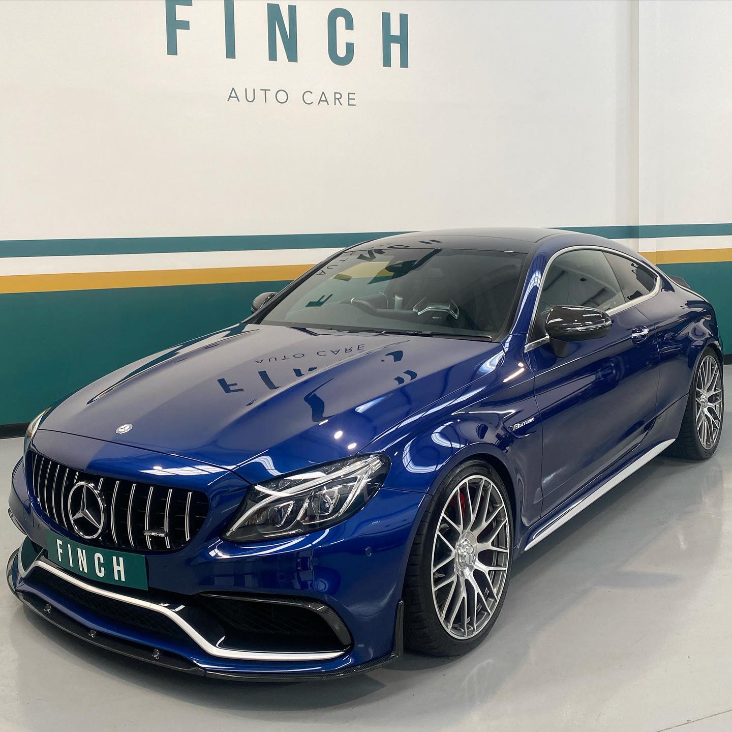 A blue mercedes-benz coupe parked inside a showroom with the sign "finch auto care" in the background.