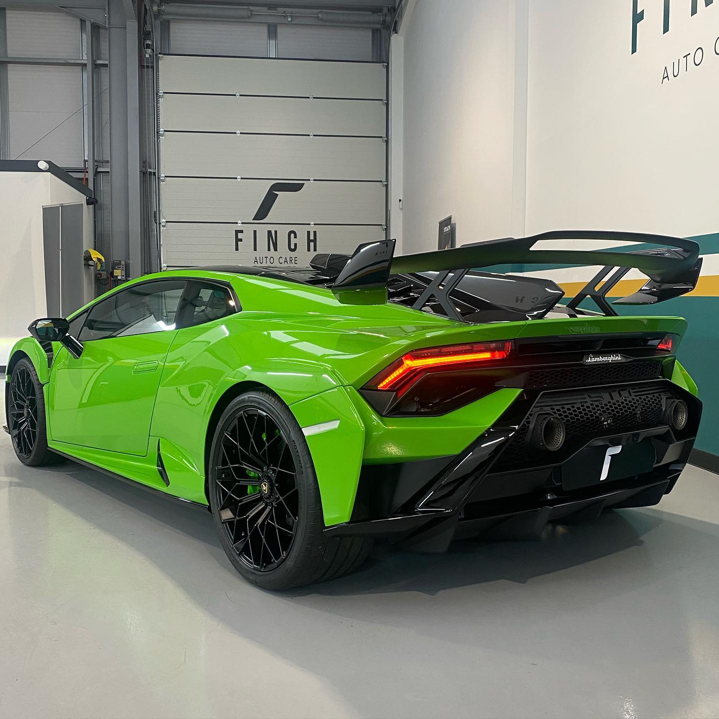 Bright green lamborghini huracán with a large rear wing parked inside a modern auto garage.
