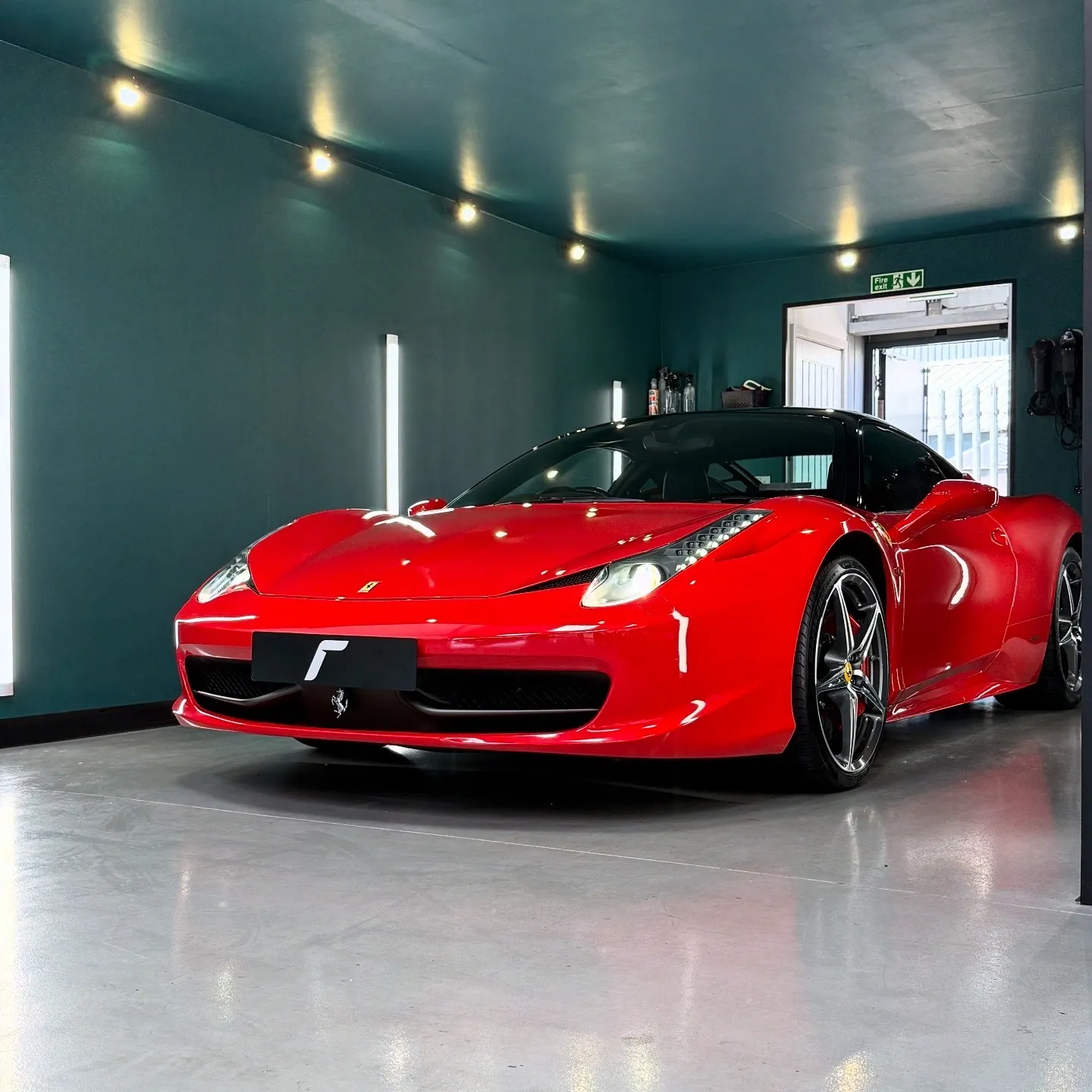 A red Ferrari sports car is parked inside a modern, well-lit garage with teal walls and polished floors.