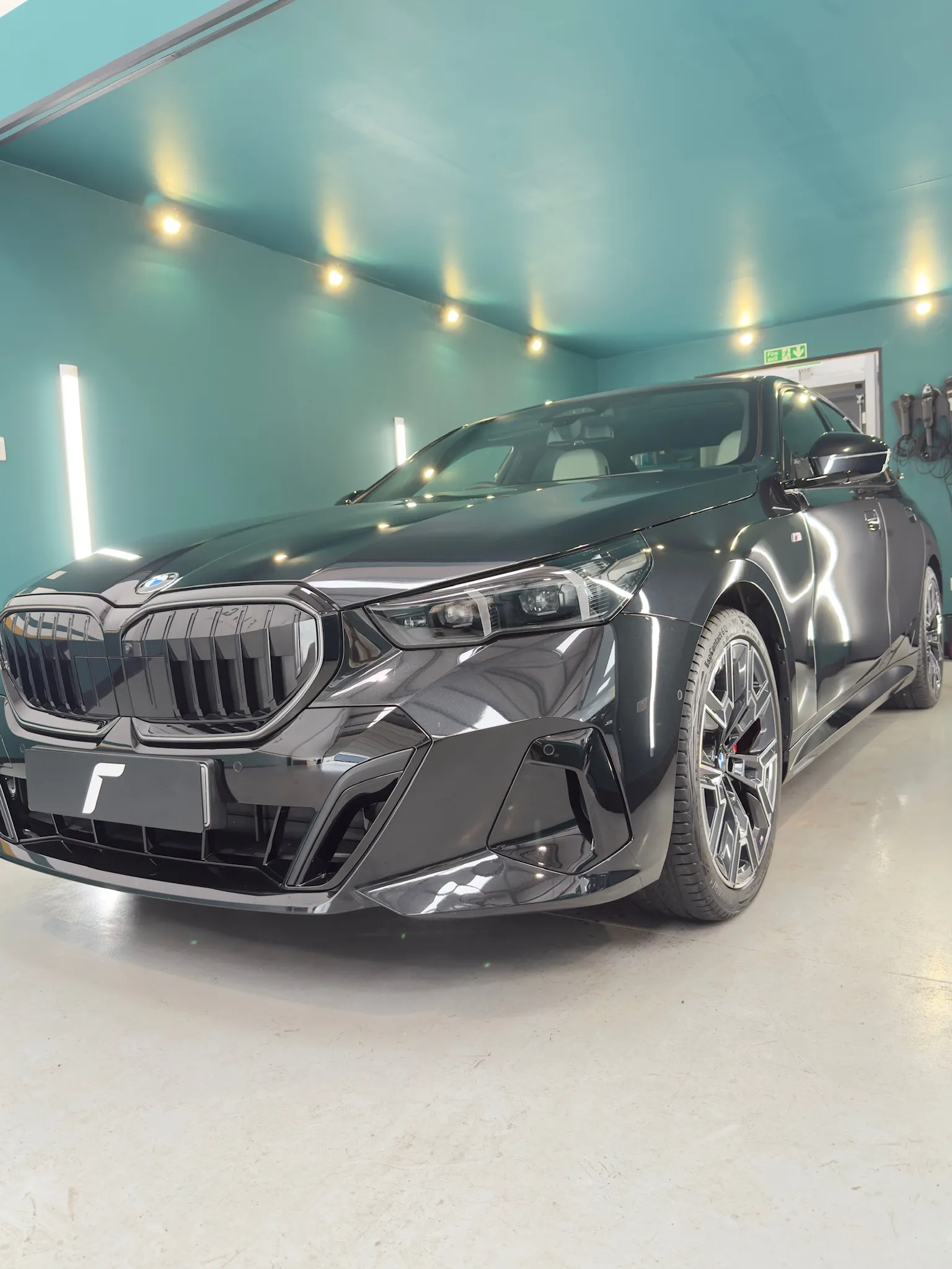 A black BMW sedan is parked inside a brightly lit garage with teal walls and ceiling.